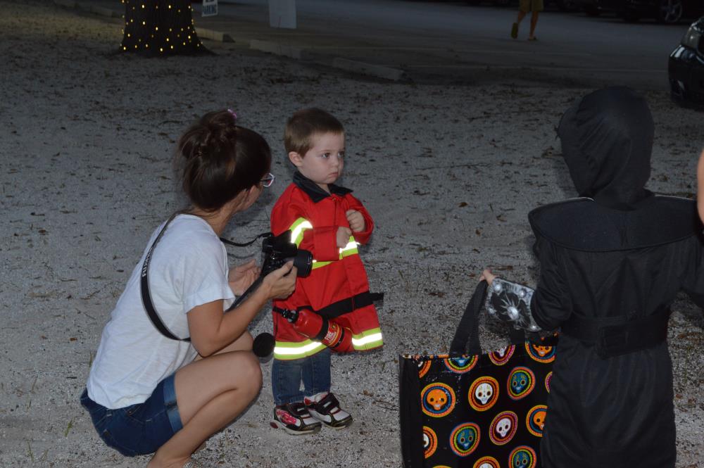 Woman with camera talks to boy dressed in red firefighter costume